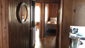 L’intérieur est en bois et un couloir mène à une chambre. Un miroir rond est accroché au mur de gauche, et on aperçoit un lit recouvert d’une couvre-lit à motifs floraux dans la pièce.