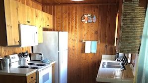 Une cuisine de taille réduite, dotée de meubles de rangement en bois, d’un réfrigérateur, d’une cuisinière et d’un évier.