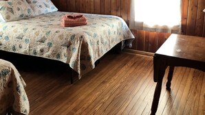 Une pièce aux murs lambrés, avec un lit, une table et une fenêtre.