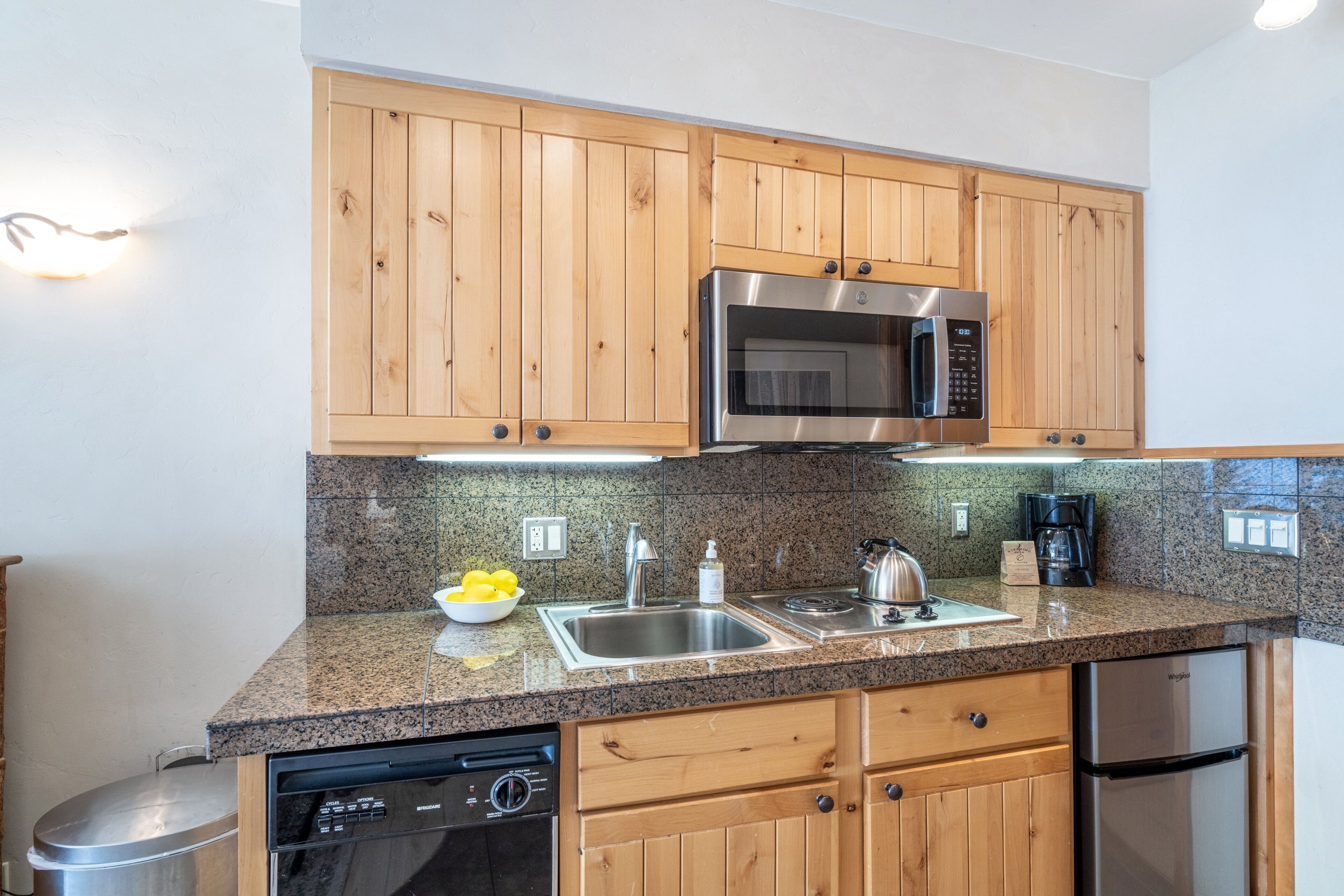 A kitchen with wooden cabinets, a stainless steel microwave, a dishwasher, and a refrigerator.