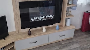 Uma sala de estar moderna com um rack de madeira para a TV, uma televisão de tela plana e objetos decorativos.
