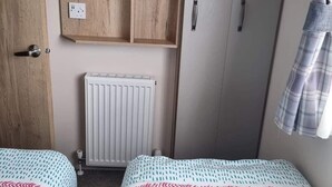 Quarto com duas camas, um guarda-roupa, um radiador e um espelho.
