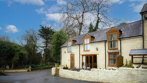 A stone building with a sloped roof, a wooden door, and windows with wooden frames. - Rose Coach House - 3 Bedroom Cottage - Pendine (Carmarthen)