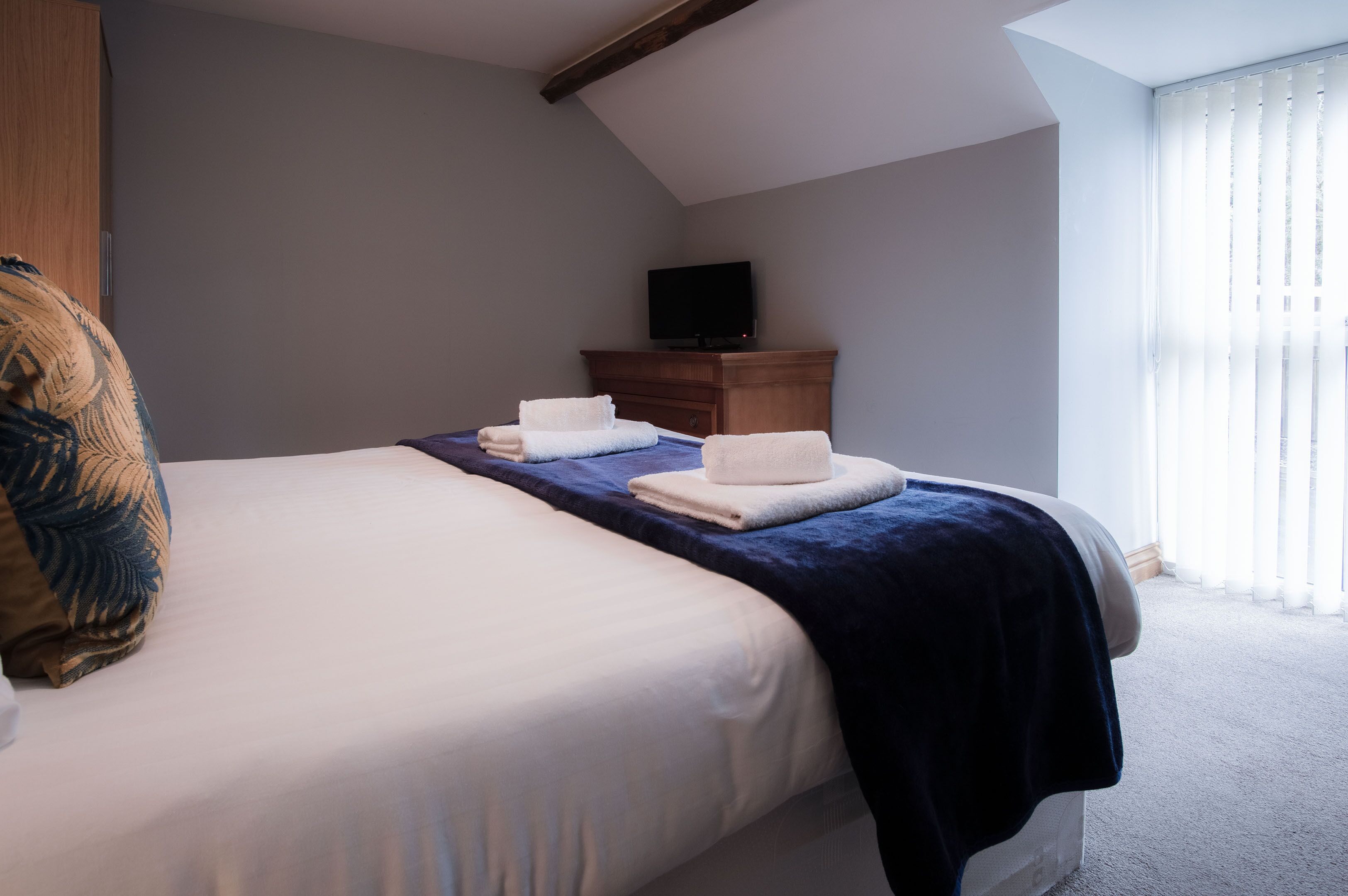 Quarto com uma cama, penteadeira de madeira e uma televisão sobre um suporte.