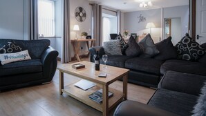 A modern living room with a sofa, coffee table, and a dining area with a table and chairs. - Rose Coach House - 3 Bedroom Cottage - Pendine (Carmarthen)
