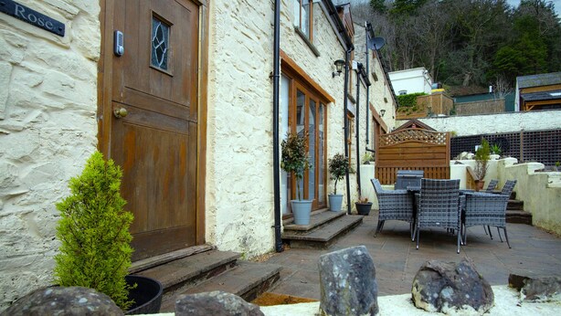 A stone building with a wooden door, outdoor seating, and potted plants. - Rose Coach House - 3 Bedroom Cottage - Pendine (Carmarthen)