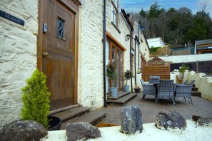 A stone building with a wooden door, outdoor seating, and potted plants. - Rose Coach House - 3 Bedroom Cottage - Pendine (Carmarthen)