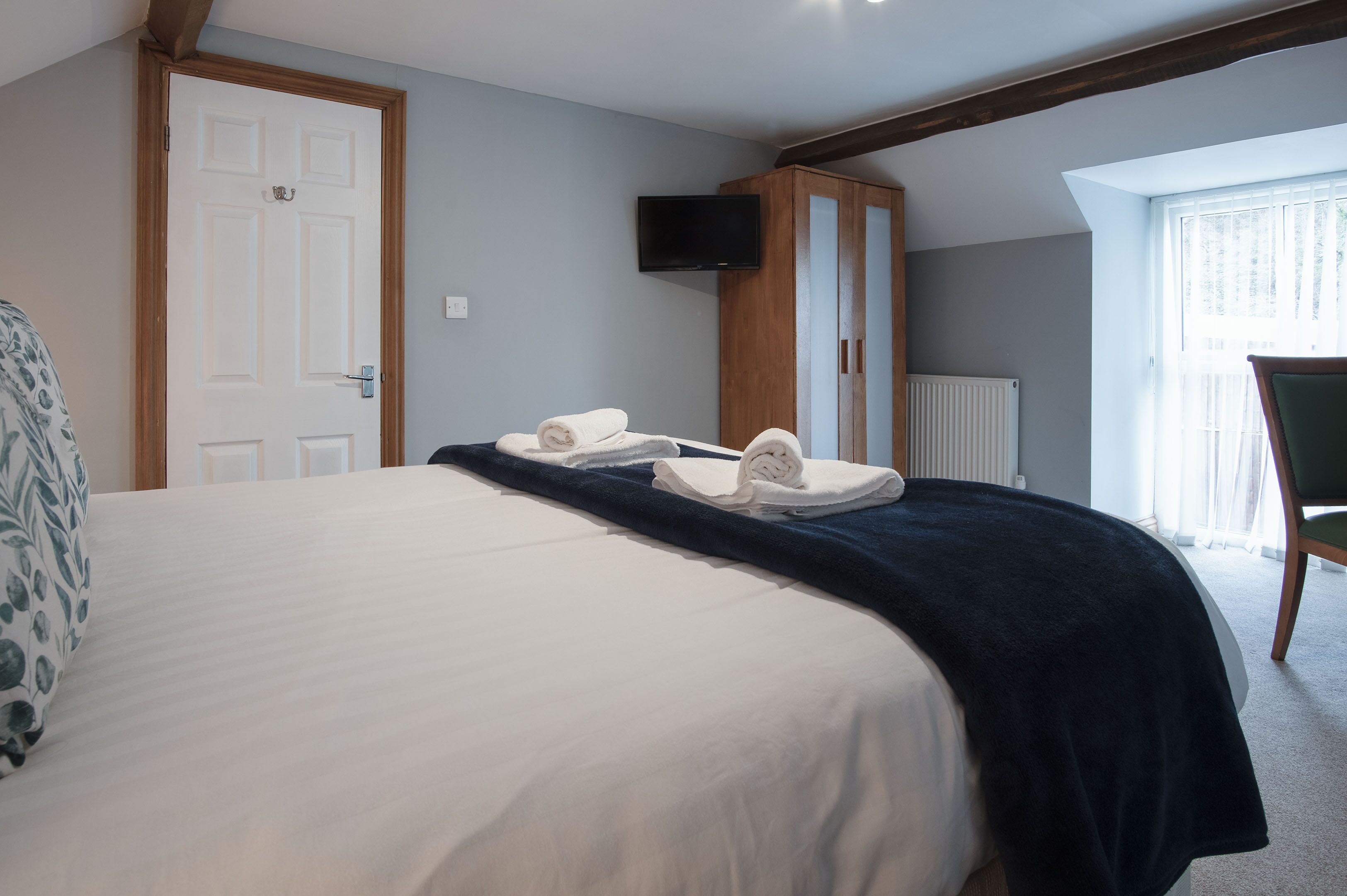 Una habitación de hotel con una cama, un televisor montado en un armario de madera y una ventana con cortinas.