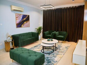 A modern living room with a green sofa, two green armchairs, a coffee table, and a painting on the wall.