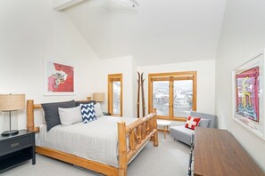 A bedroom with a bed, a wooden bench, a desk, and a chair. There are two windows and a view of a snowy landscape. - Mountain Village Panoramic Views, Hot Tub, Fireplace 3 Bedroom Townhouse by RedAwning (Telluride)