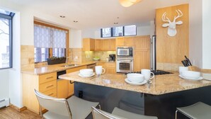 Une cuisine moderne dotée de plans de travail en granit, d’armoires en bois, d’un four encastré et d’un grand îlot central avec des places assises.