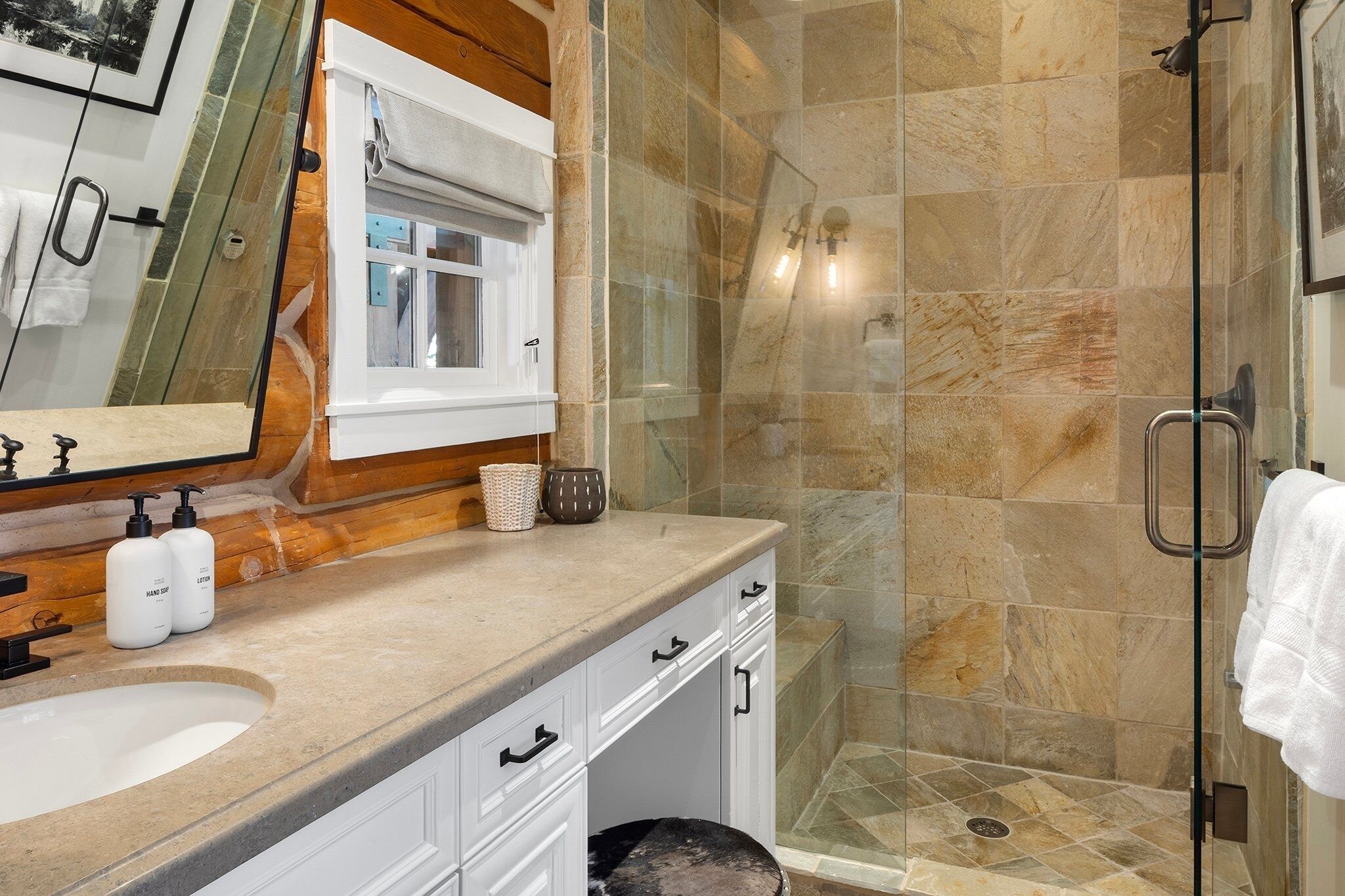 A bathroom with a glass-enclosed shower, a sink, and a mirror.