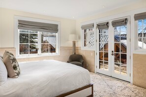 Une chambre à coucher avec un lit, une chaise, une lampe et une vue sur l’extérieur grâce à de grandes portes-fenêtres.