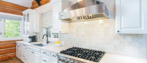 A modern kitchen with white cabinetry, a stainless steel range hood, and a gas stove.