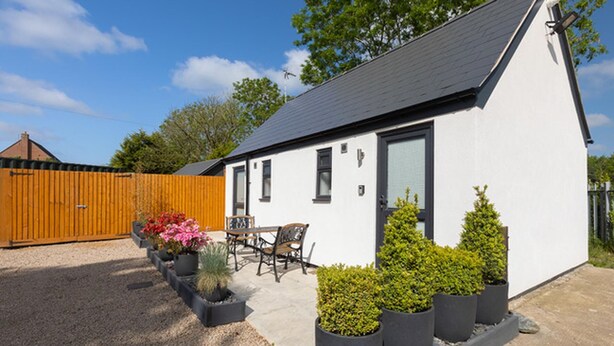A single-story white house with a dark roof, a wooden fence, and a patio with a table and chairs. - Cosy Double or Twin Studio Near Shearsby, England (Lutterworth)