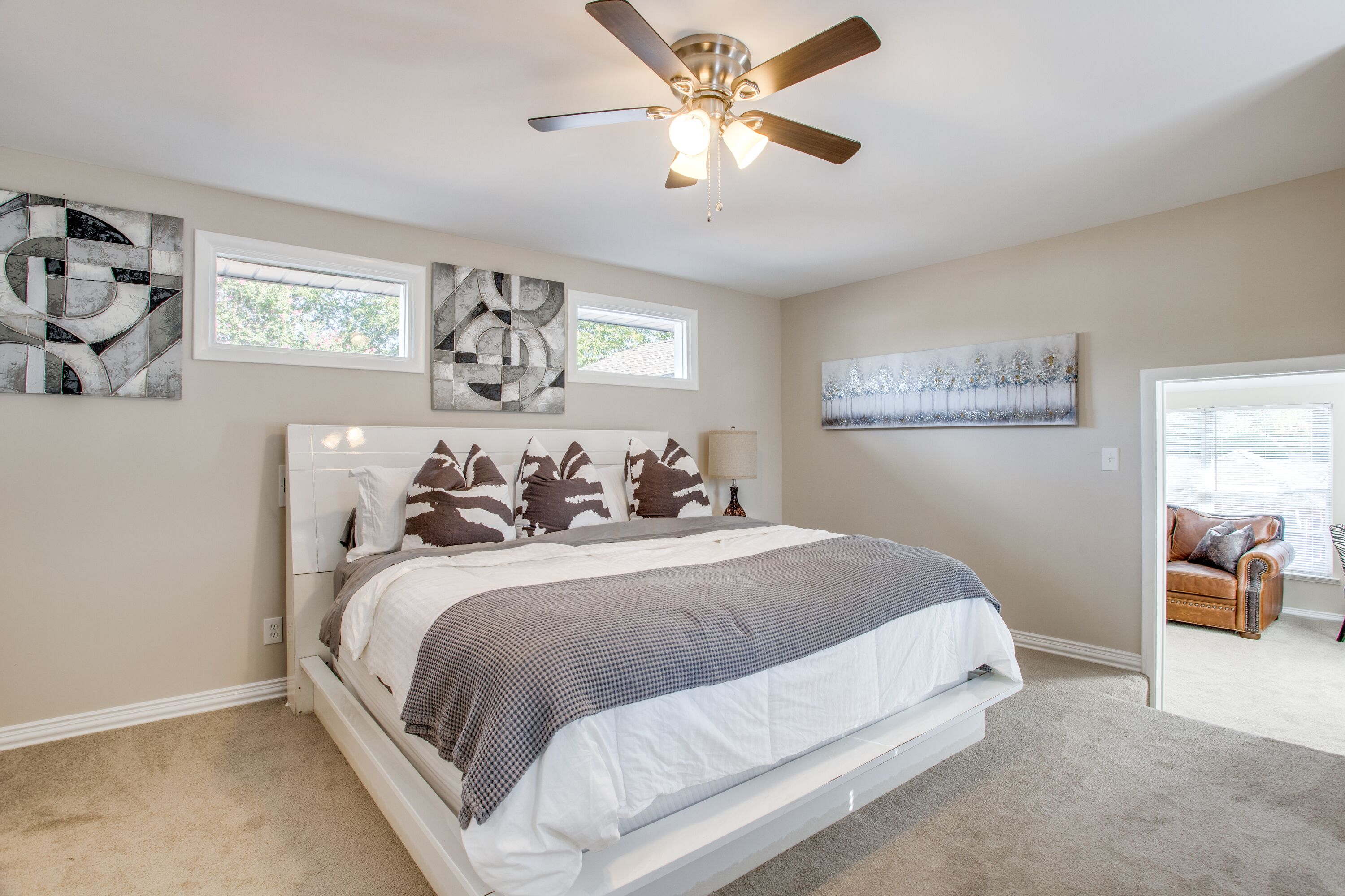 A bedroom with a large bed, ceiling fan, and artwork on the walls.
