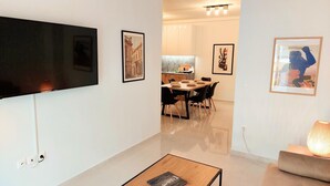 A modern living room with a flat-screen TV mounted on the wall, a dining area with a table and chairs, and a kitchen visible through an open doorway. - Wonderful Apartment in Acropolis (Athens)