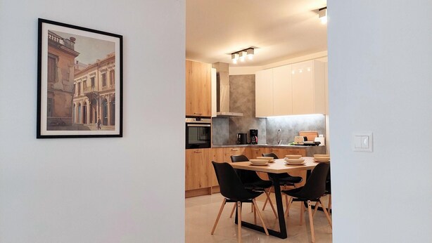 A modern kitchen with wooden cabinets, a dining table with four chairs, and a framed painting on the wall. - Wonderful Apartment in Acropolis (Athens)