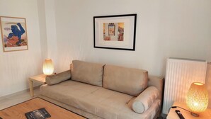 A living room with a beige sofa, two side tables with lamps, a framed picture on the wall, and a radiator. - Wonderful Apartment in Acropolis (Athens)