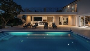 Una casa moderna con piscina, mobiliario exterior y balcón.