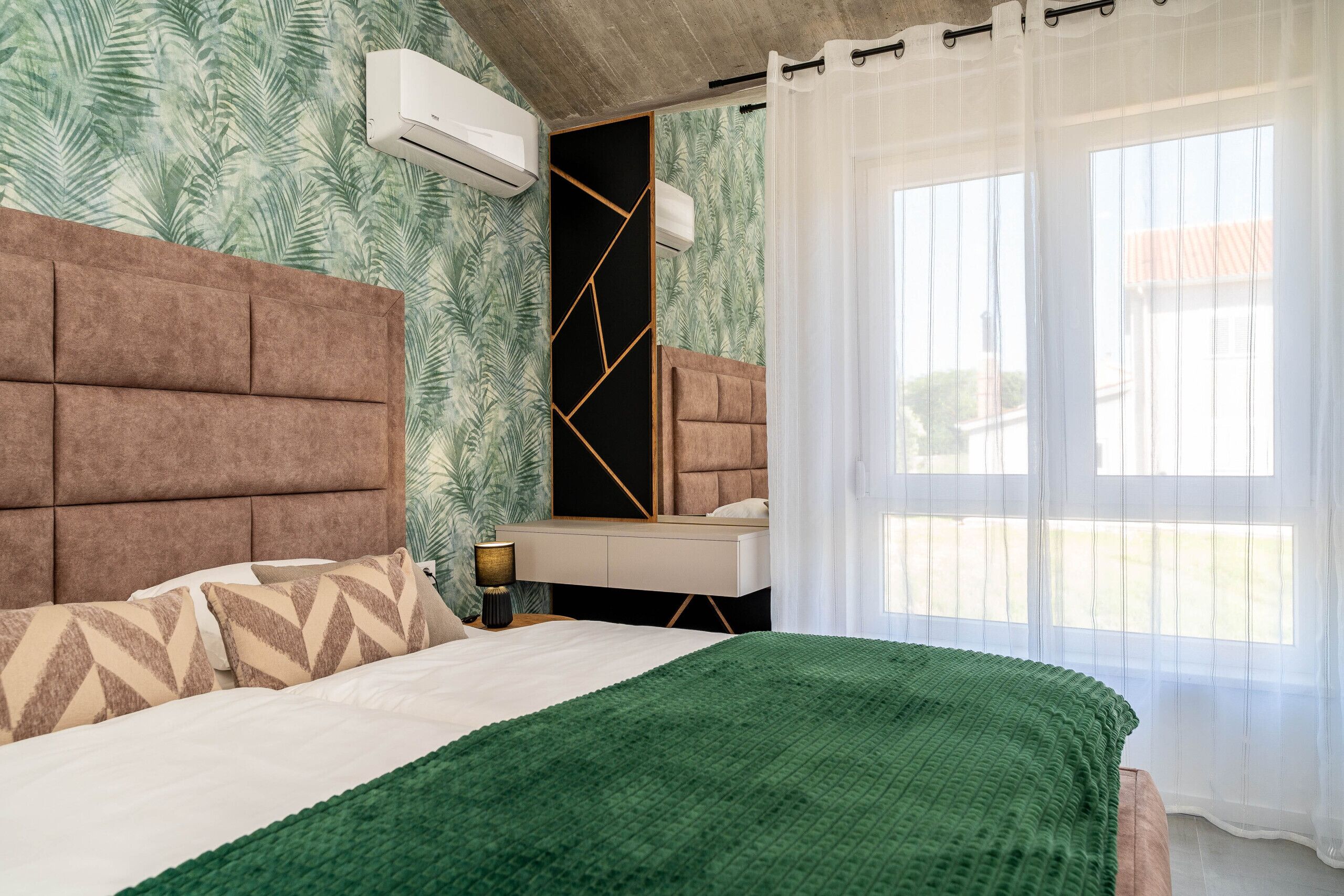 A bedroom with a bed, a bedside table, a mirror, and a window with curtains.