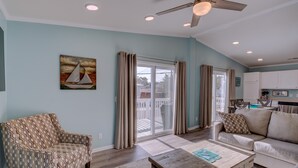 A spacious living room with a patterned armchair, a sofa, and a wooden coffee table. A ceiling fan and recessed lighting are visible.