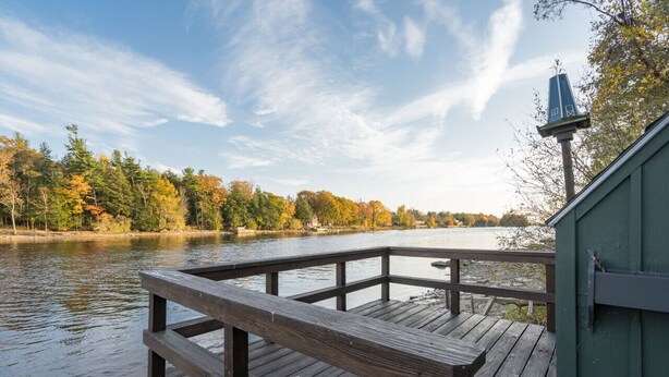 Une jetée en bois s’étendant au-dessus d’une rivière paisible, entourée d’arbres aux couleurs automnales.