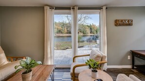 Un salon avec vue sur un lac, une table basse en bois, un canapé et un panneau indiquant le mot « LAC ».