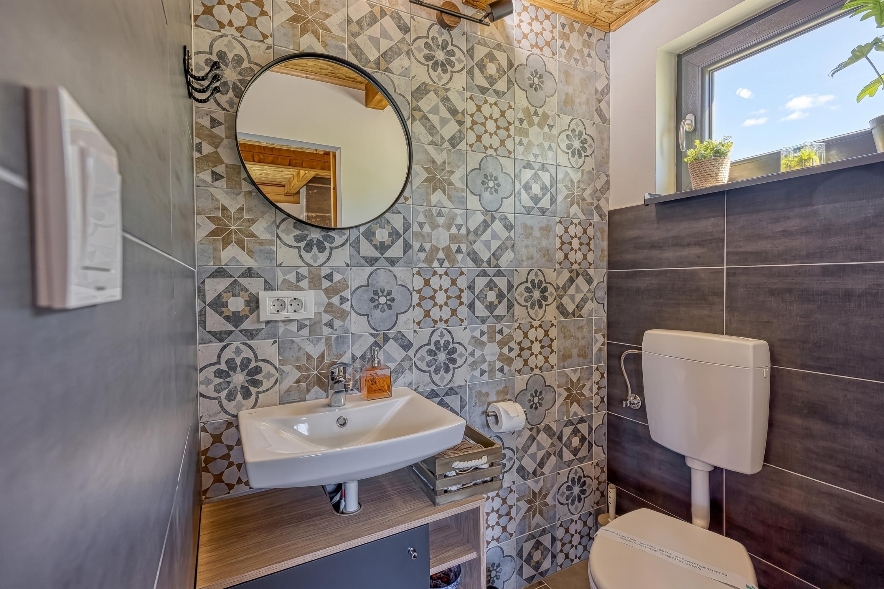 Een badkamer met een wastafel, spiegel, toilet en betegeling met een patroon.