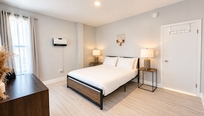 Un dormitorio moderno con una cama grande, mesitas de noche, aire acondicionado instalado en la pared y una puerta con perchero.