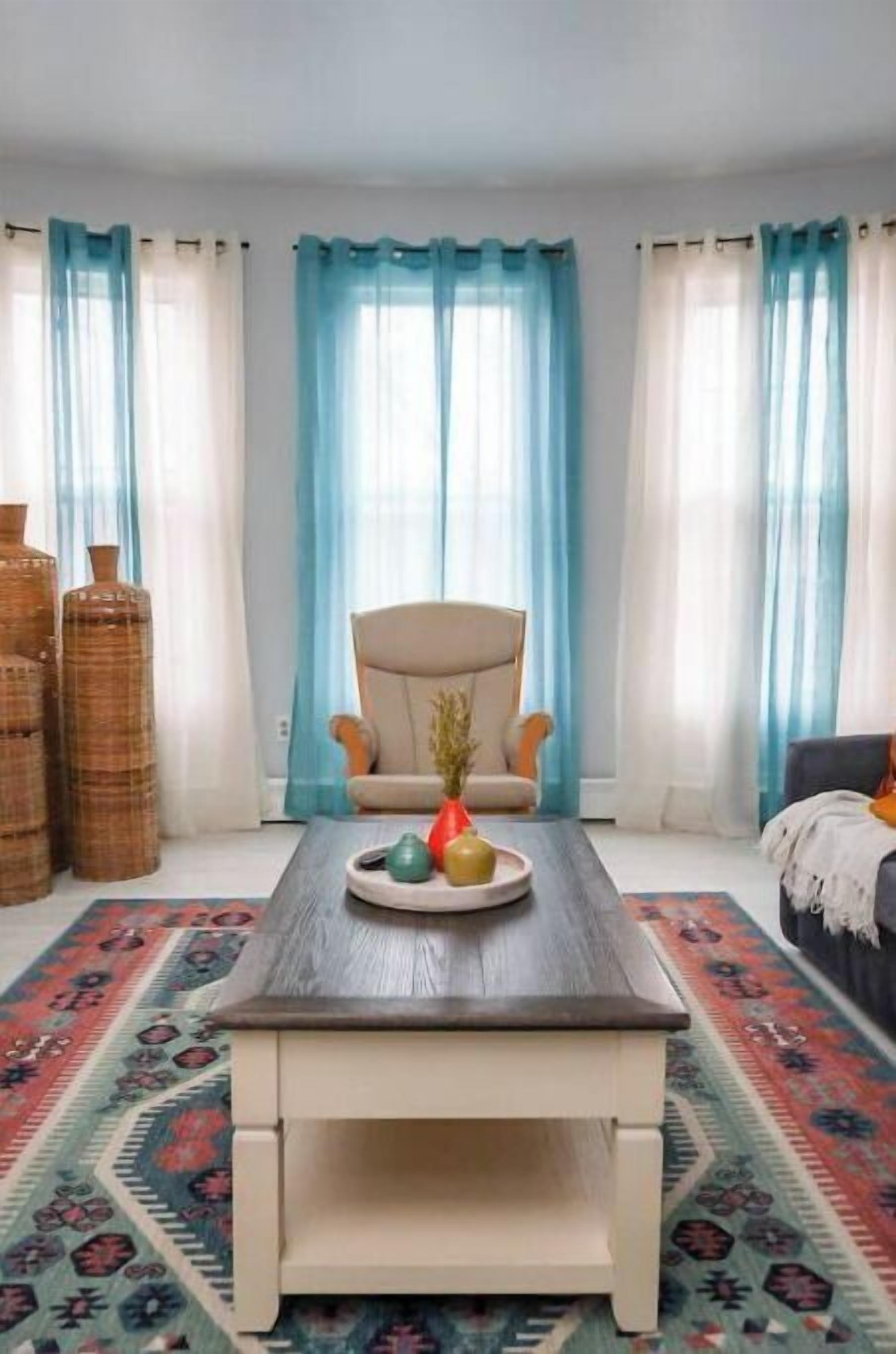 Ein Wohnzimmer mit einem dunklen Holztisch, einem beigen Sessel und einem farbenfrohen Teppich.