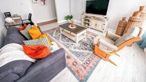 Un soggiorno moderno con un divano grigio, un tavolino in legno, una poltrona beige e una TV su un mobile bianco.