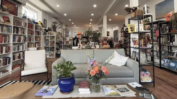 Un accogliente soggiorno con un divano grigio, un tavolino da caffè con libri e un vaso di fiori, ed elementi decorativi e librerie piene di libri.