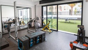 A gym with weightlifting equipment, exercise bikes, and a large window with a view of a courtyard. - Sunset 302 Apt de Luxe Avec Salle de Fitness (Tunis)