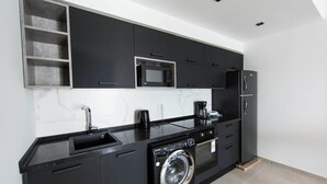 A modern kitchen with black cabinetry, a built-in microwave, a coffee maker, a washing machine, and a sink. - Sunset 302 Apt de Luxe Avec Salle de Fitness (Tunis)