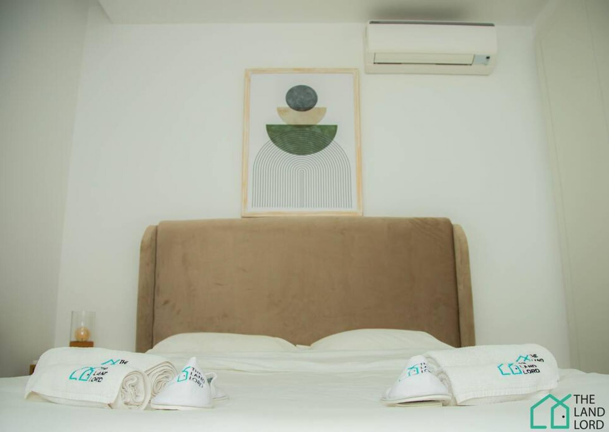Una habitación de hotel con cama, aire acondicionado de pared y una obra de arte enmarcada sobre la cama.