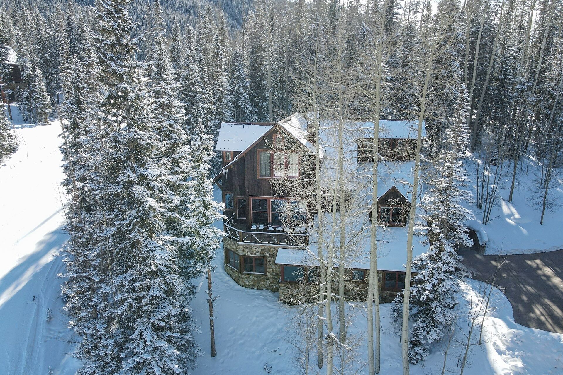 Een houten chalet omgeven door met sneeuw bedekte bomen, met een stenen fundering en een balkon.