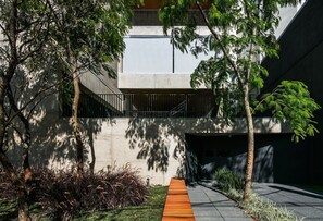 A modern building with a concrete facade, a wooden pathway, and surrounding greenery. - Huma Klabin (São Paulo)