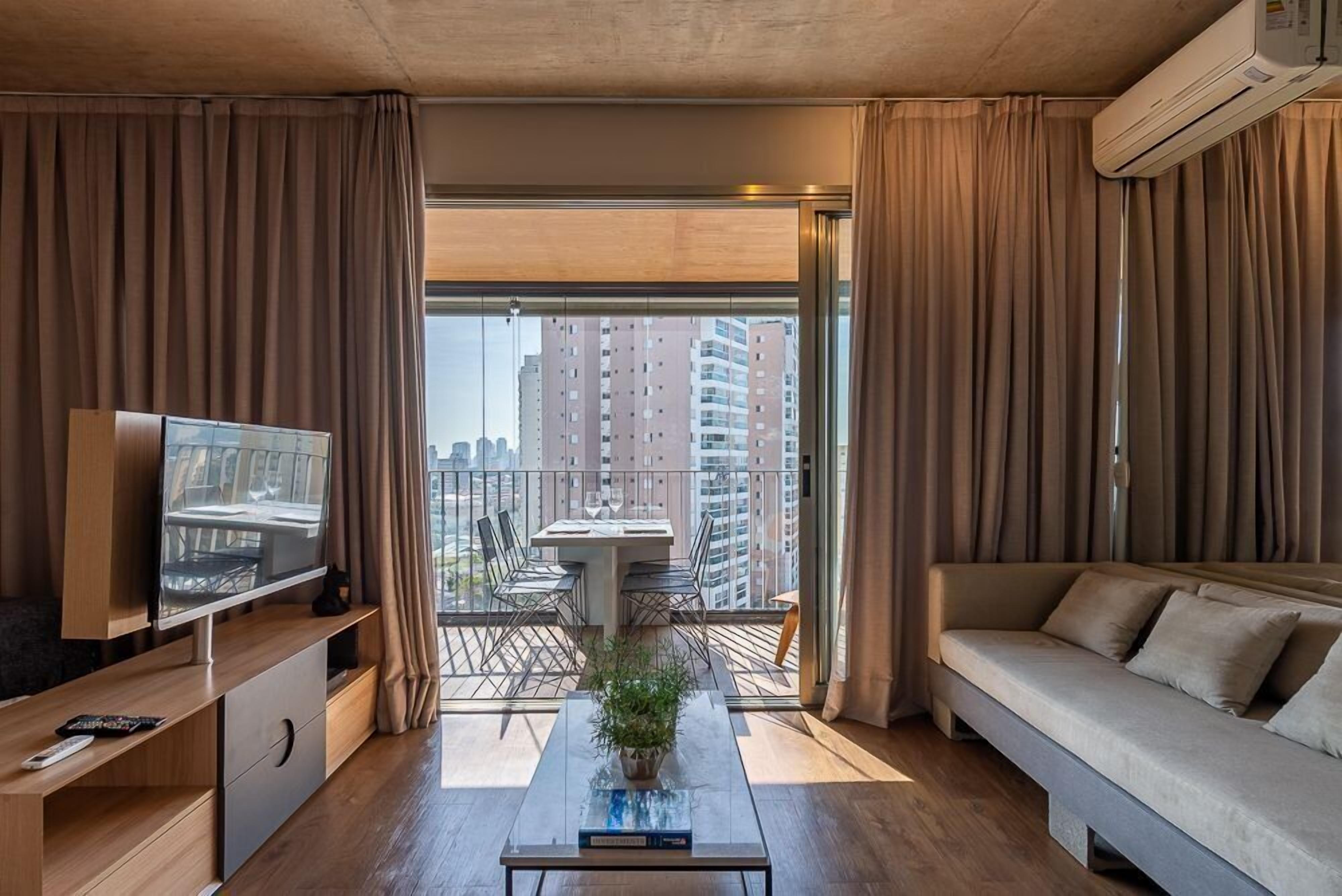 A modern living room with a flat-screen TV, a sofa, a coffee table with a plant, and a balcony with a table and chairs.