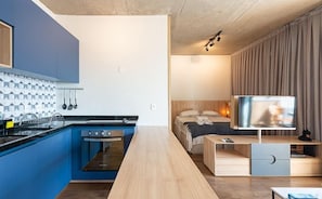 Una habitación de hotel moderna con espacio para cocinar, una cama con televisor y un escritorio de madera.