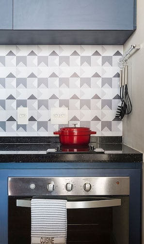 A kitchen with a gas stove, a red pot, and a backsplash with geometric tiles.