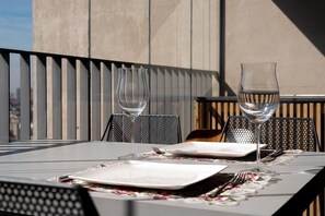 A table set for two with two wine glasses and a plate, set against a modern building facade. - Huma Klabin (São Paulo)