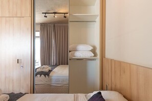 Habitación de hotel con cama, armario y espejo que refleja la habitación.