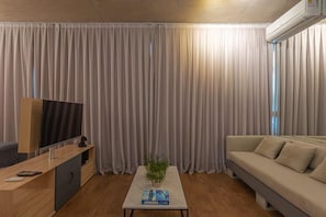 Una sala de estar moderna con un televisor de pantalla plana, una consola de madera, un sofá color beige y una planta en una mesa de centro.