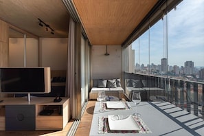 A modern apartment with a balcony, a dining area, a TV, and a city view.