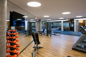 A modern gym with wooden flooring, exercise equipment, and large windows.