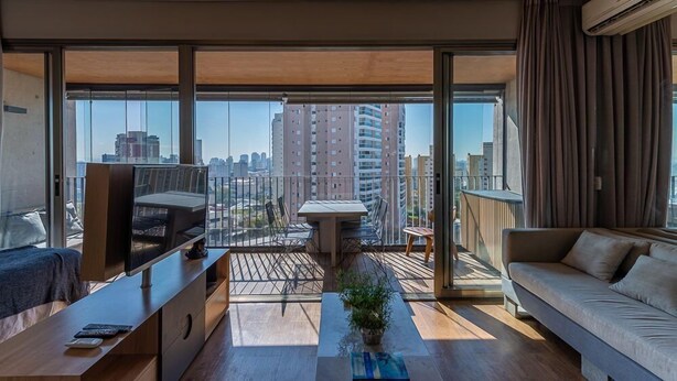 A modern living room with a large TV, a sofa, a dining area, and a balcony with a city view. - Huma Klabin (São Paulo)