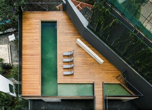 A rooftop pool area with a wooden deck, a long swimming pool, and a seating area with lounge chairs.