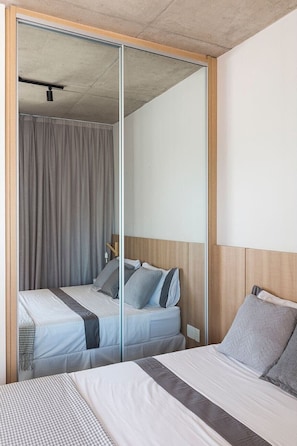 A bedroom with a mirrored wardrobe, a bed with grey bedding, and a wooden headboard.