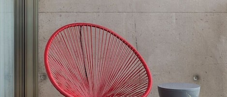 A red chair and a grey table against a concrete wall with a wooden floor.